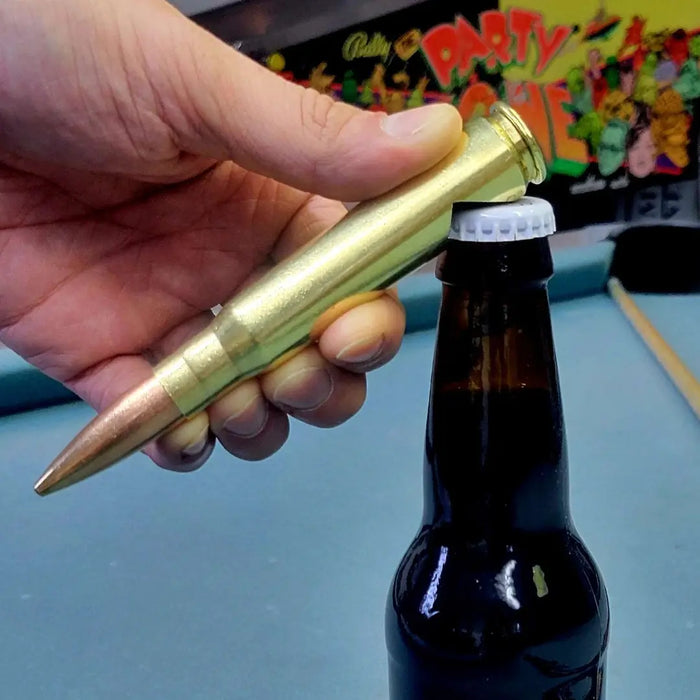 50 caliber bmg brass bullet bottle opener opening beer bottle on pool table with pinball machine in background