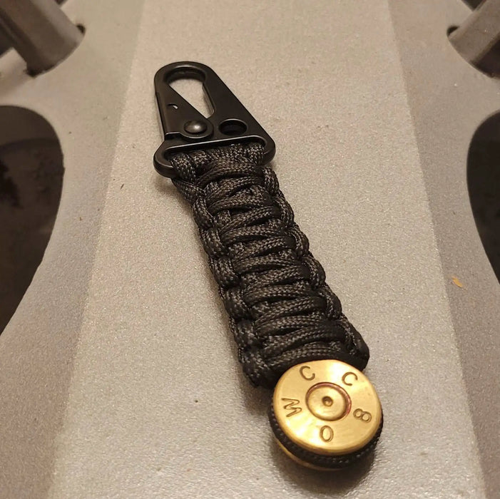 50 Bmg Bullet Paracord Keychain with black paracord and heavy duty hk style clasp sitting on t34 tank engine block