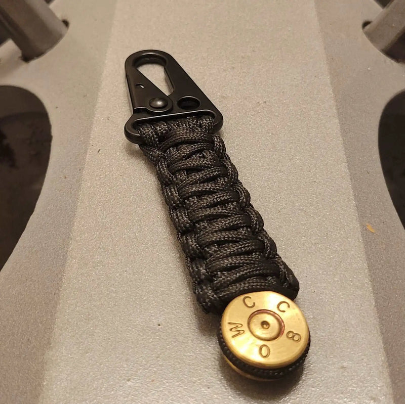 50 Bmg Bullet Paracord Keychain with black paracord and heavy duty hk style clasp sitting on t34 tank engine block 