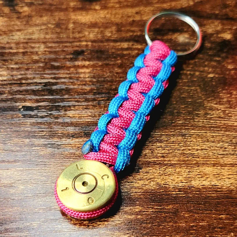 Neon blue and pink paracord 50 bmg bullet keychain sitting on desk